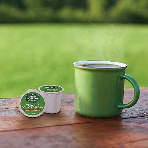 A green coffee mug and Green Mountain pods on a wooden table outdoors